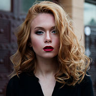 Portrait of a confident woman with curly blonde hair and bold makeup.