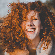 Smiling woman with curly red hair in natural light.