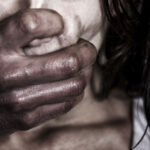 A hand covering a person's mouth in a dark, distressing scene.