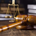 A wooden judge's gavel and brass scales of justice on a desk.