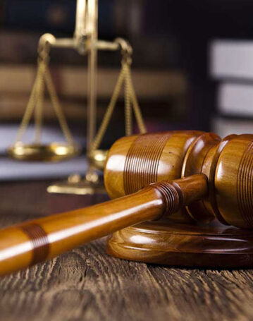 A wooden judge's gavel and brass scales of justice on a desk.