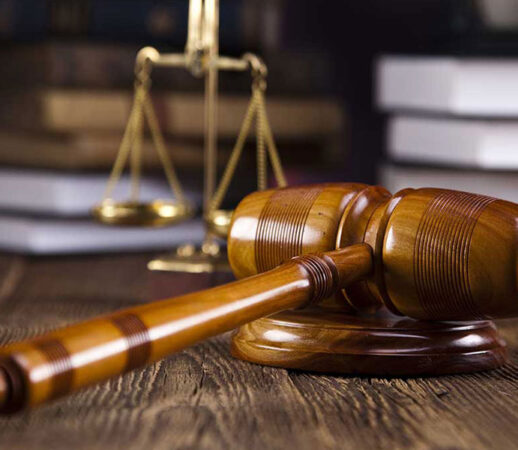 A wooden judge's gavel and brass scales of justice on a desk.