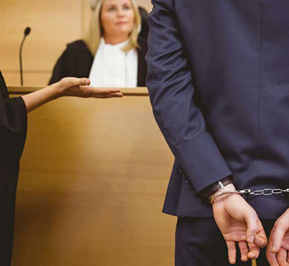 A man in handcuffs stands before a judge in a courtroom.
