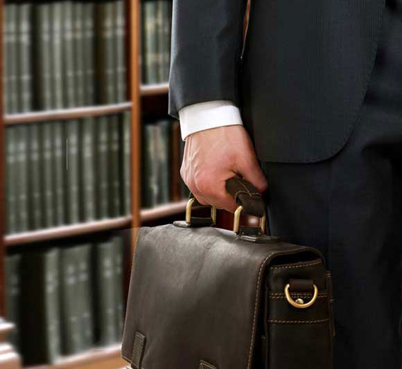 Businessman holding a leather briefcase in a library or office.