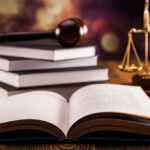 Open law book with gavel and scales of justice in the background.