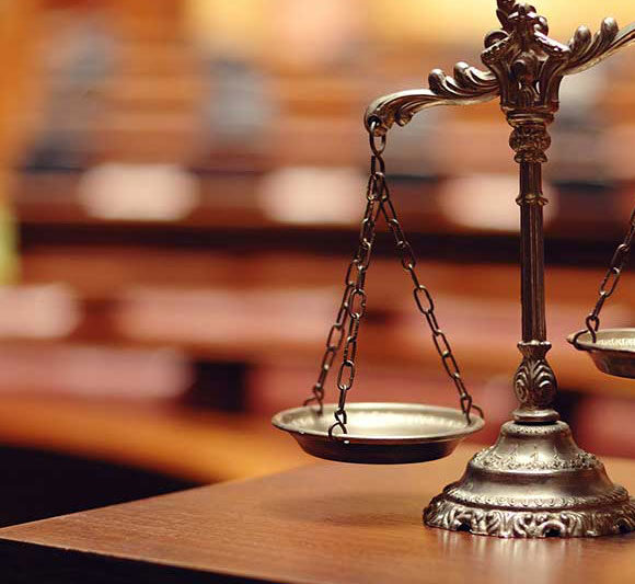 Close-up of a vintage balance scale on a wooden desk in a courtroom.
