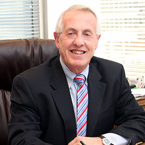 Smiling man in a suit sitting at a desk in an office.