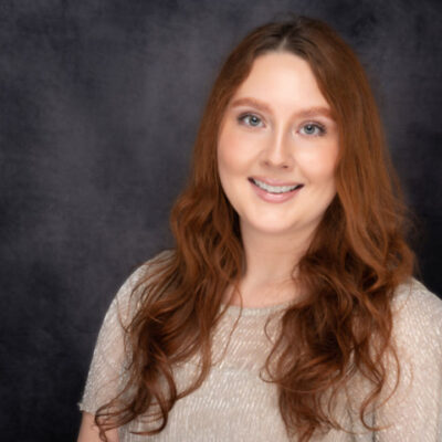 Smiling woman with long red hair in front of a dark background.