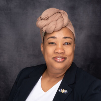 Professional woman smiling, wearing a beige headwrap and dark blazer. Professional woman smiling, wearing a beige headwrap and dark blazer.