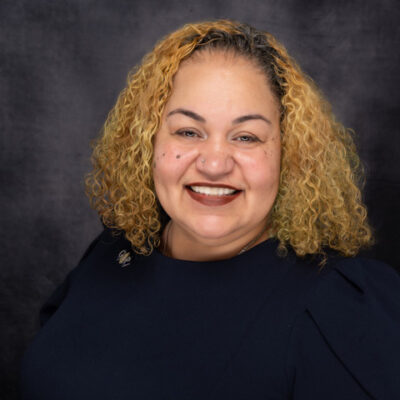 Smiling woman with curly blonde hair against a dark backdrop. Smiling woman with curly blonde hair against a dark backdrop.