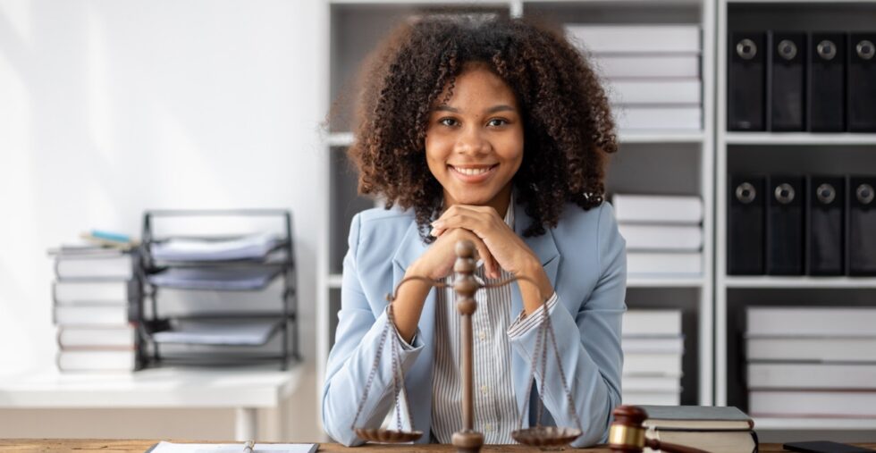 Confident female judge smiling in courtroom with gavel and law books.